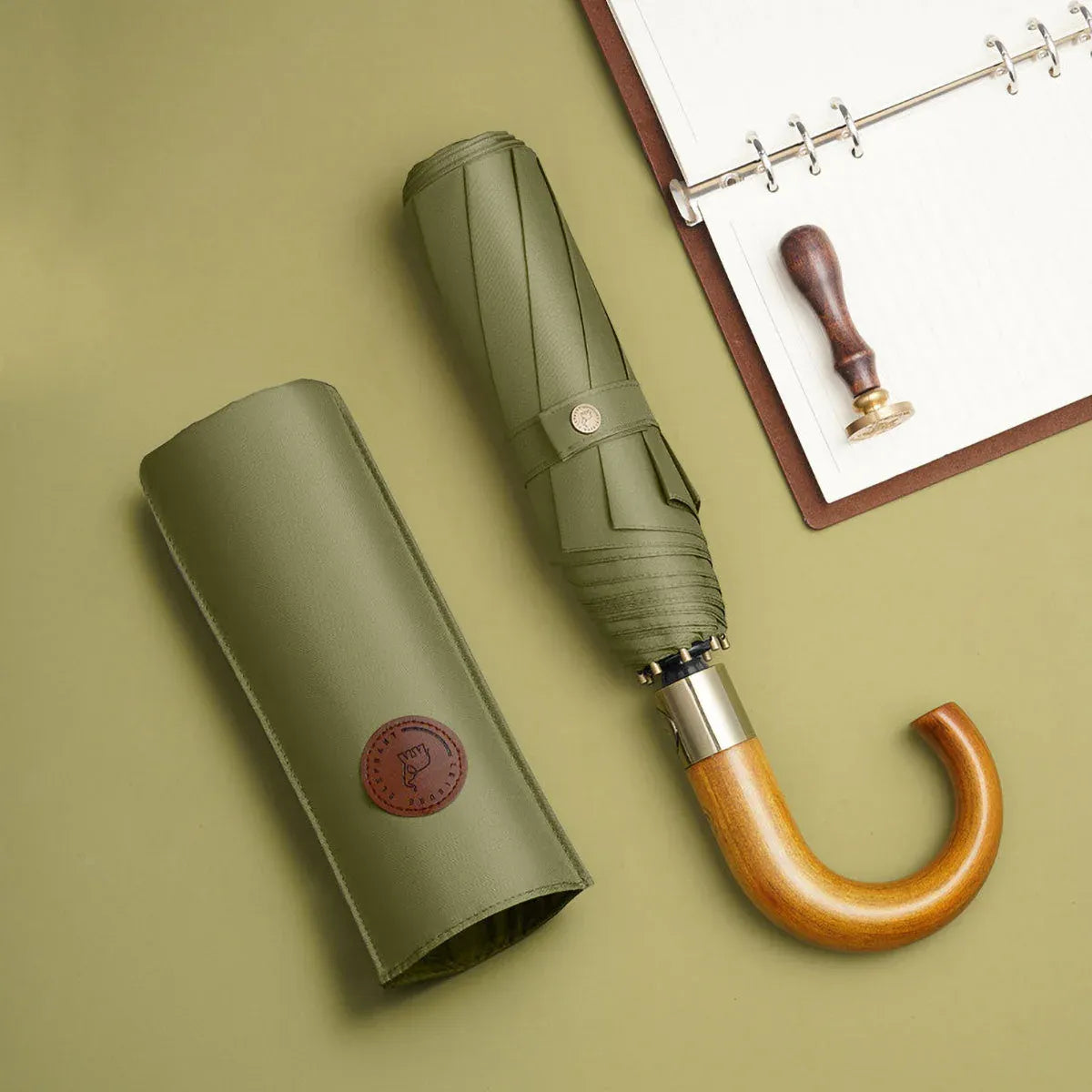 The classic storm proof folding umbrella in olive green, shown closed with its matching leather sleeve.
