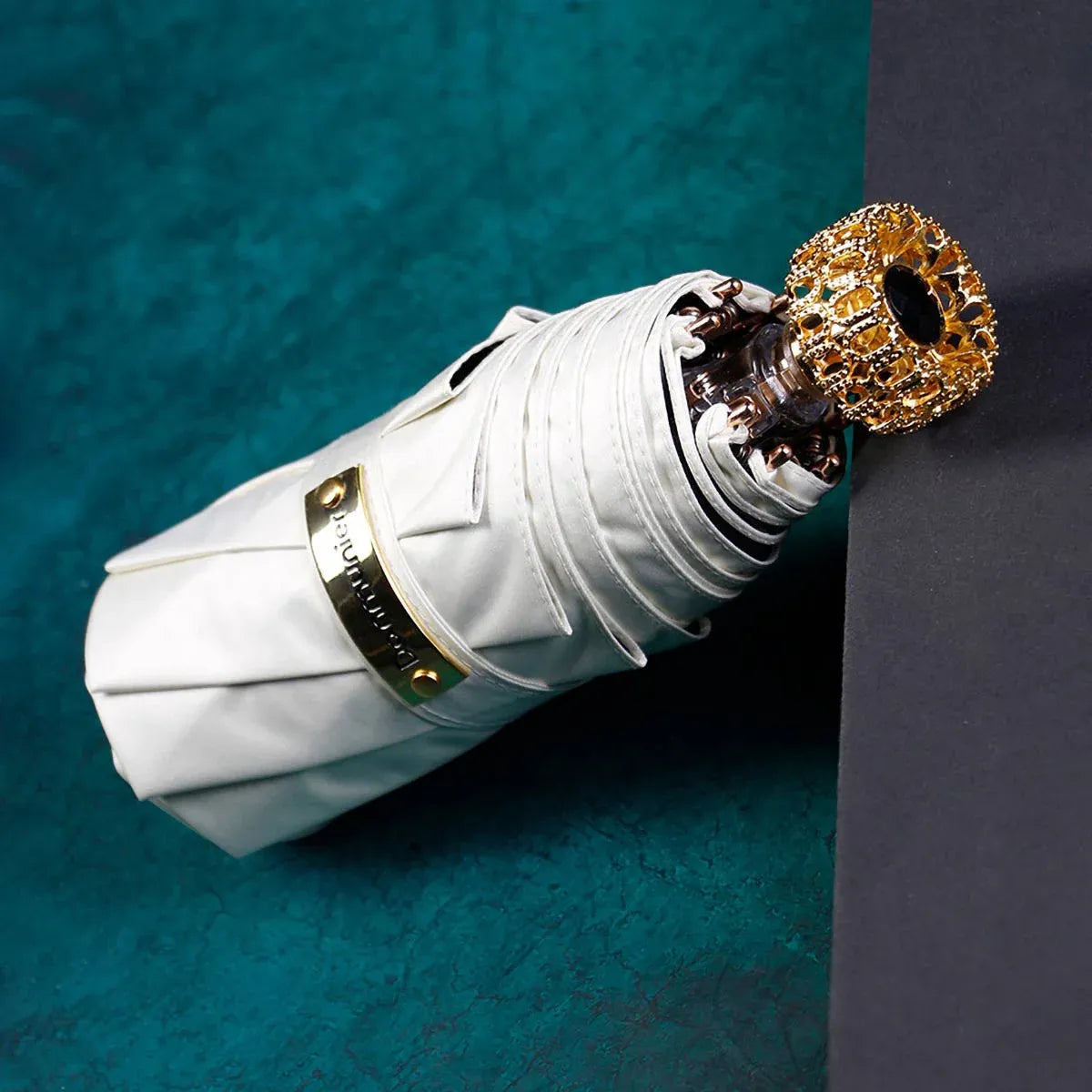 The compact luxury mini umbrella in white, showcasing the ornate golden handle with a black crystal.