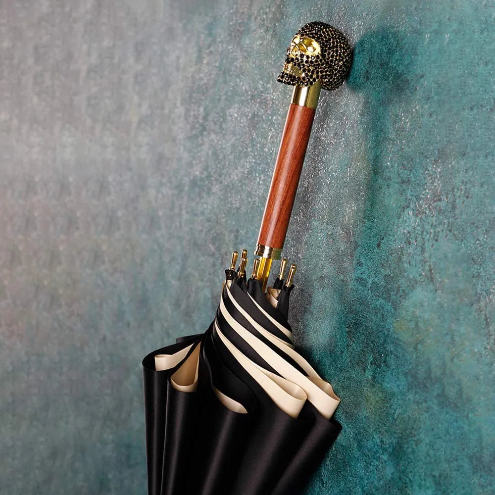 The black Diamond Skull stick umbrella leaning against a wall, showcasing the jeweled skull handle.