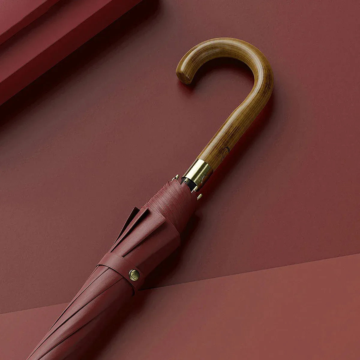 The elegant classic stick umbrella with a natural wooden crook handle, shown closed in dark red.