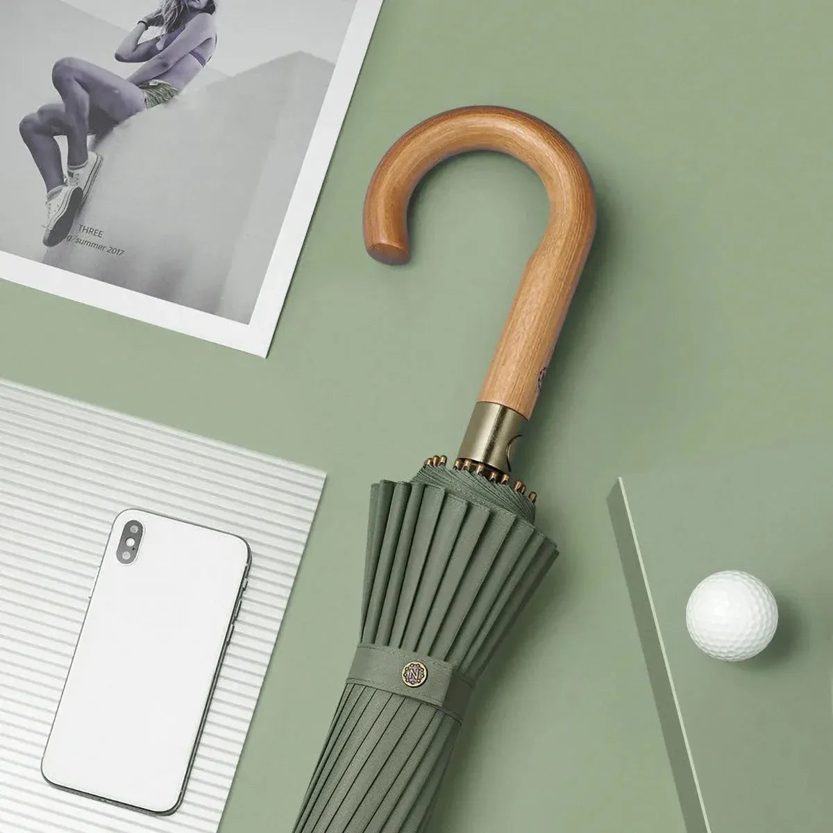 Lifestyle shot of the closed strong windproof 24-rib umbrella in green with its natural wood crook handle.