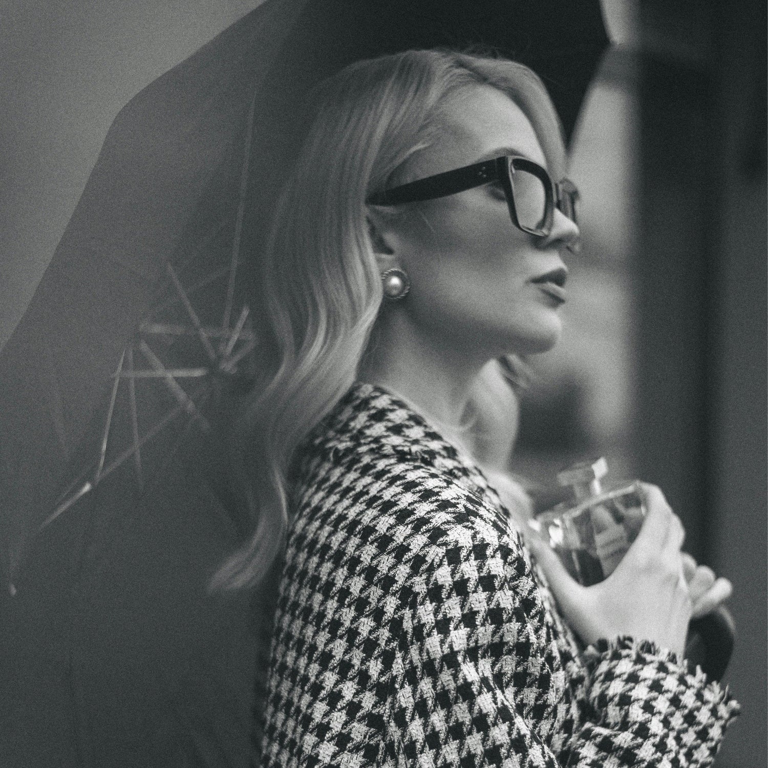 A sophisticated woman in a houndstooth coat holding an umbrella, symbolizing Exclusaro’s elegant and timeless rainwear for women.