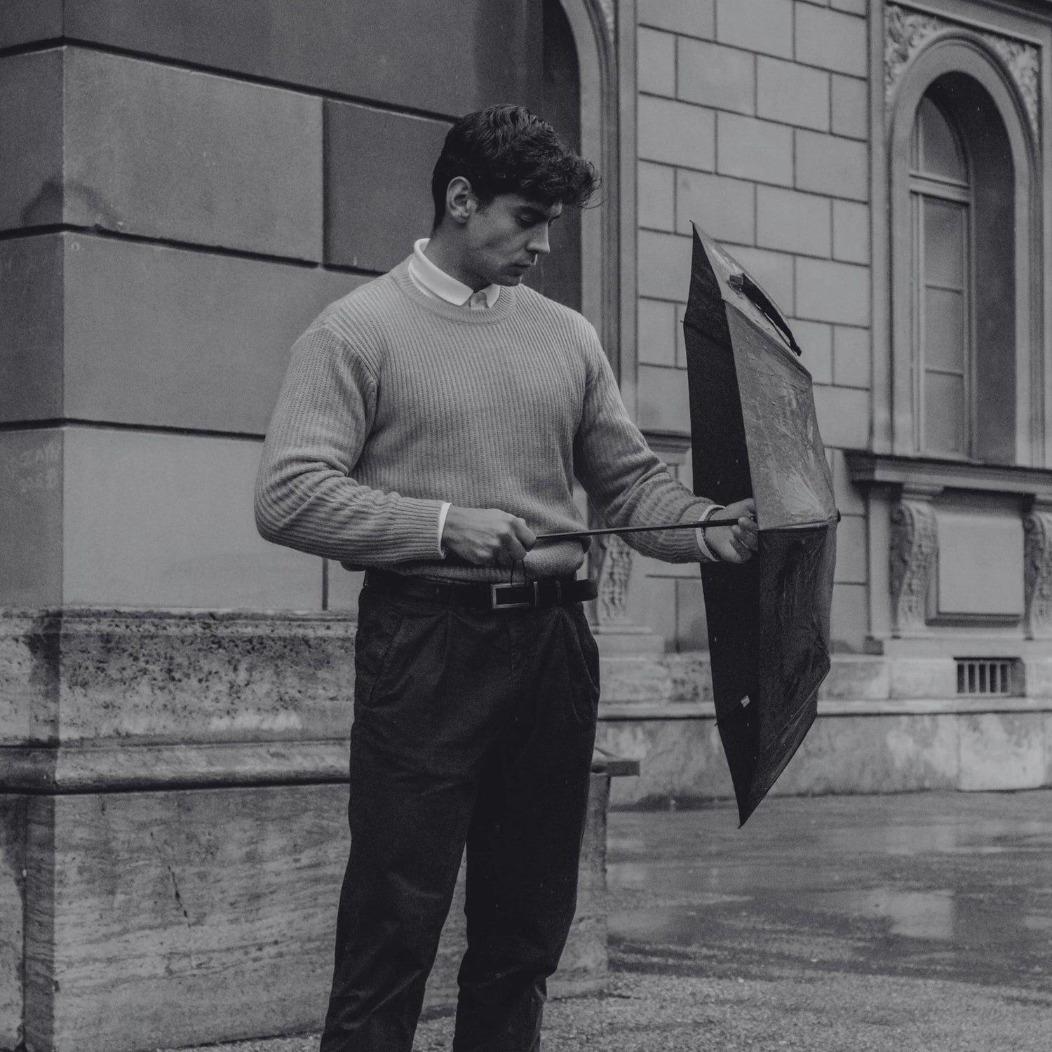 A modern gentleman adjusting his umbrella on a rainy day, representing Exclusaro’s refined and durable luxury umbrellas for men.