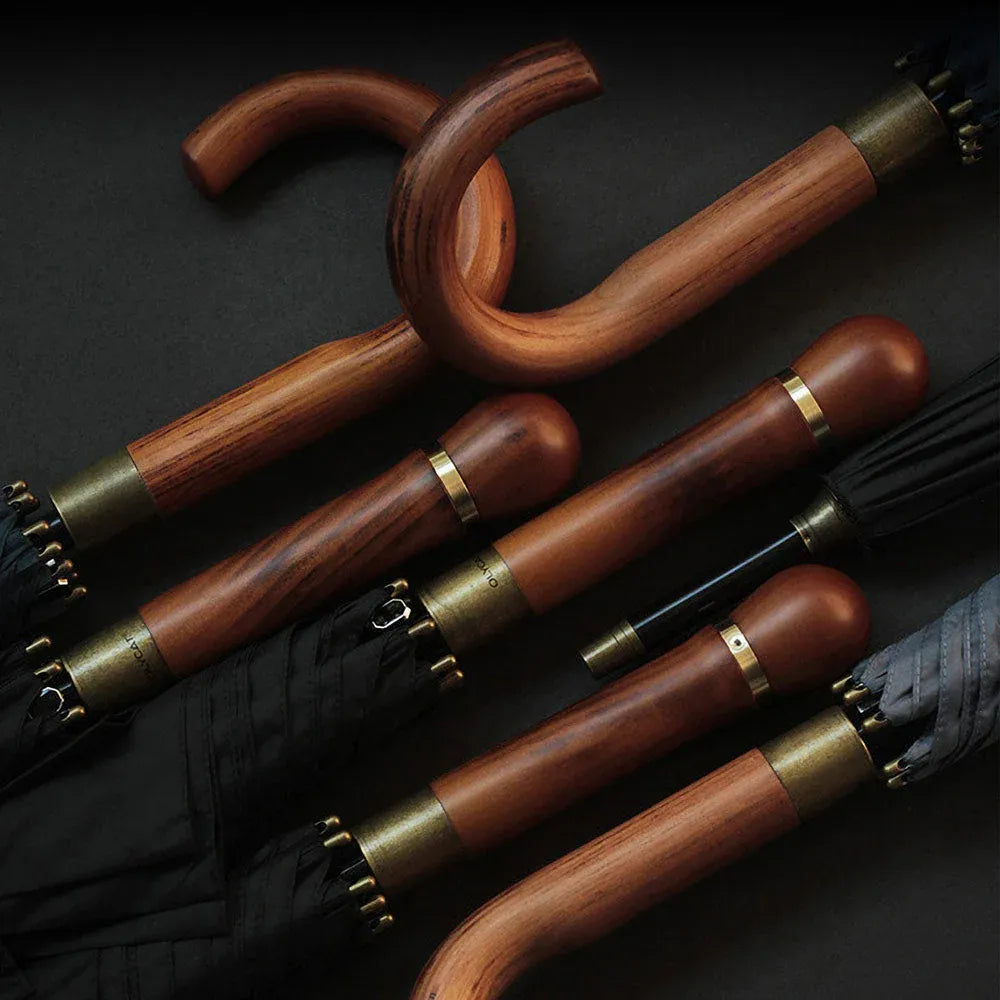 Collection of luxury umbrellas with solid wood handles and brass details on dark background.