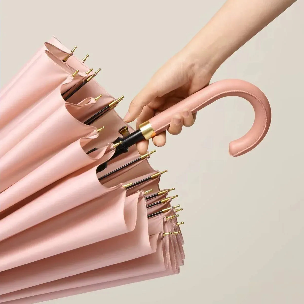 A woman's hand holding the comfortable pink leather crook handle of the 24-rib ladies storm umbrella.