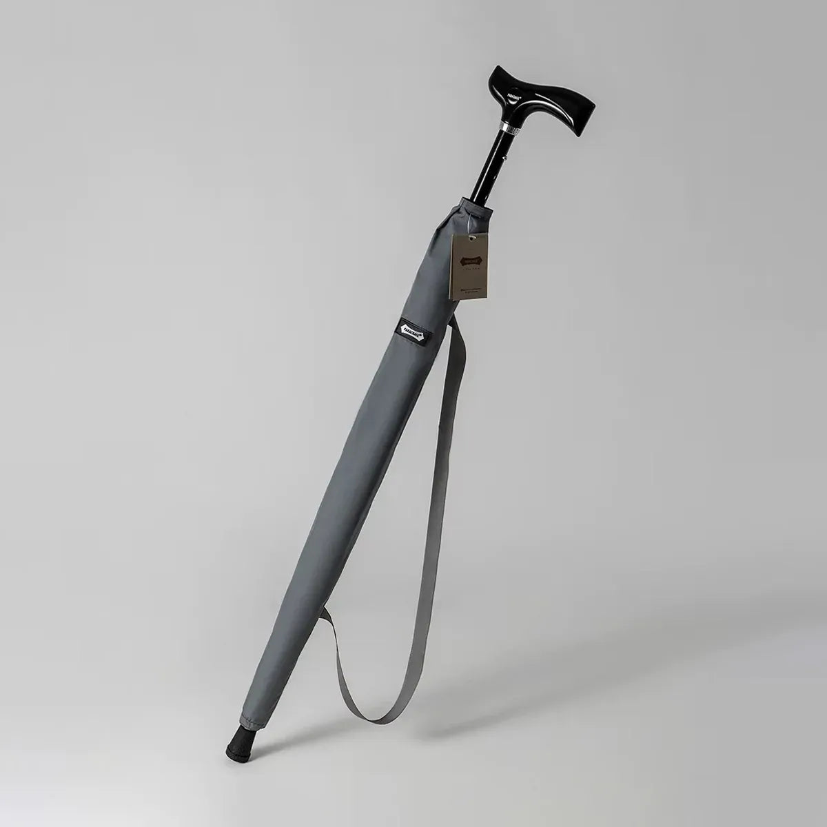 The adjustable walking stick umbrella in grey, shown in its carrying sleeve with a shoulder strap.