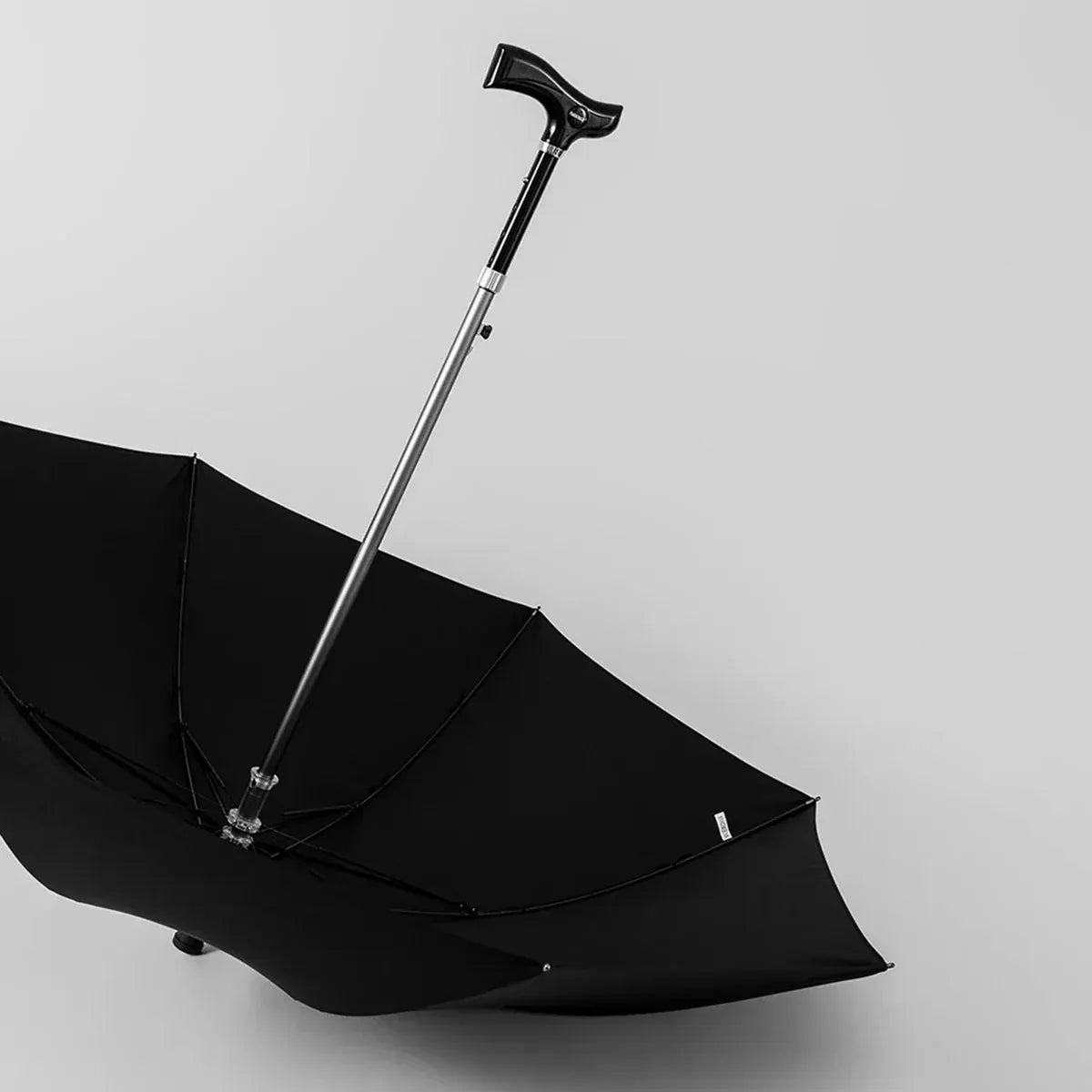 The open black walking stick umbrella resting on the floor, highlighting the adjustable shaft.