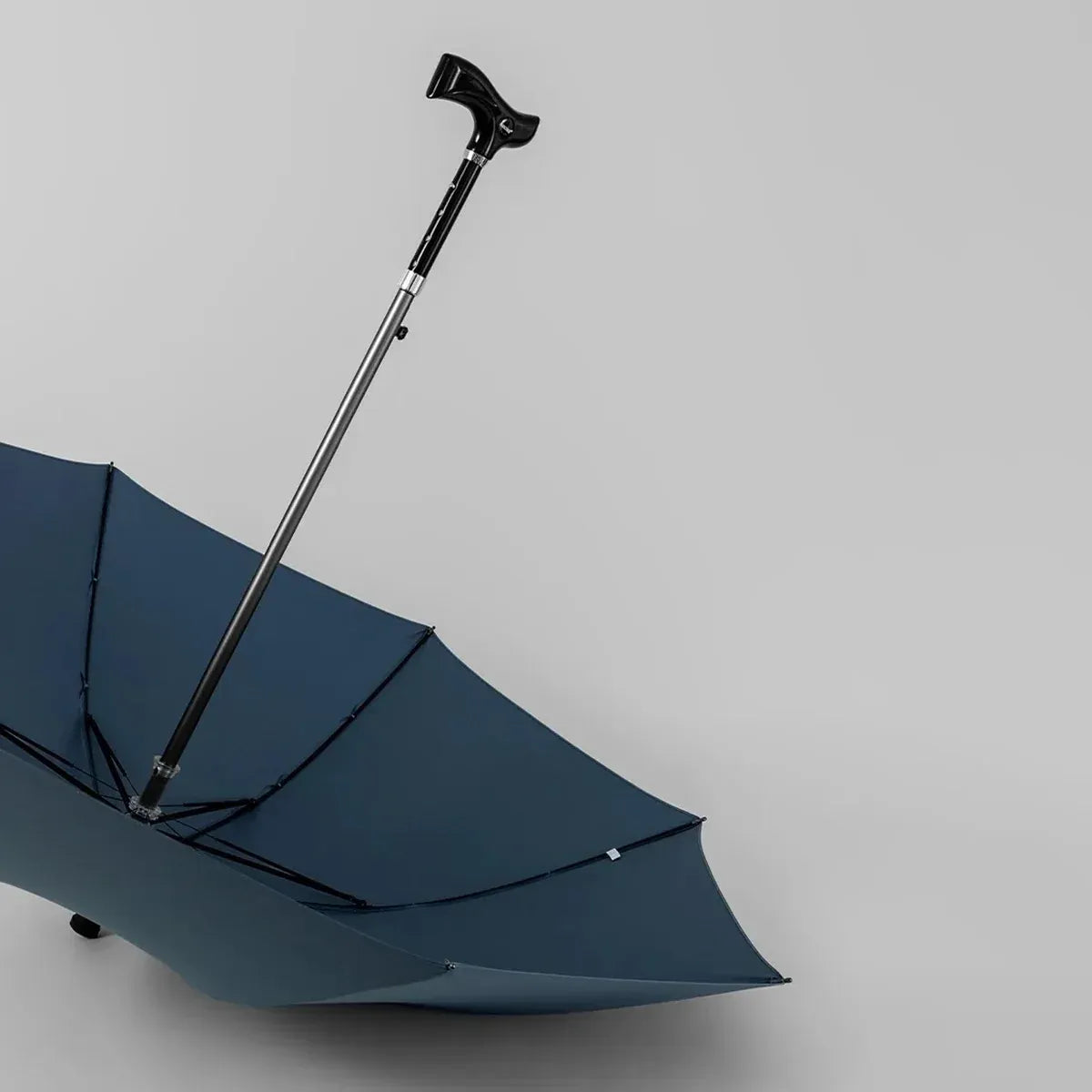 The open navy blue walking stick umbrella resting on the floor, showing its full canopy and derby handle.
