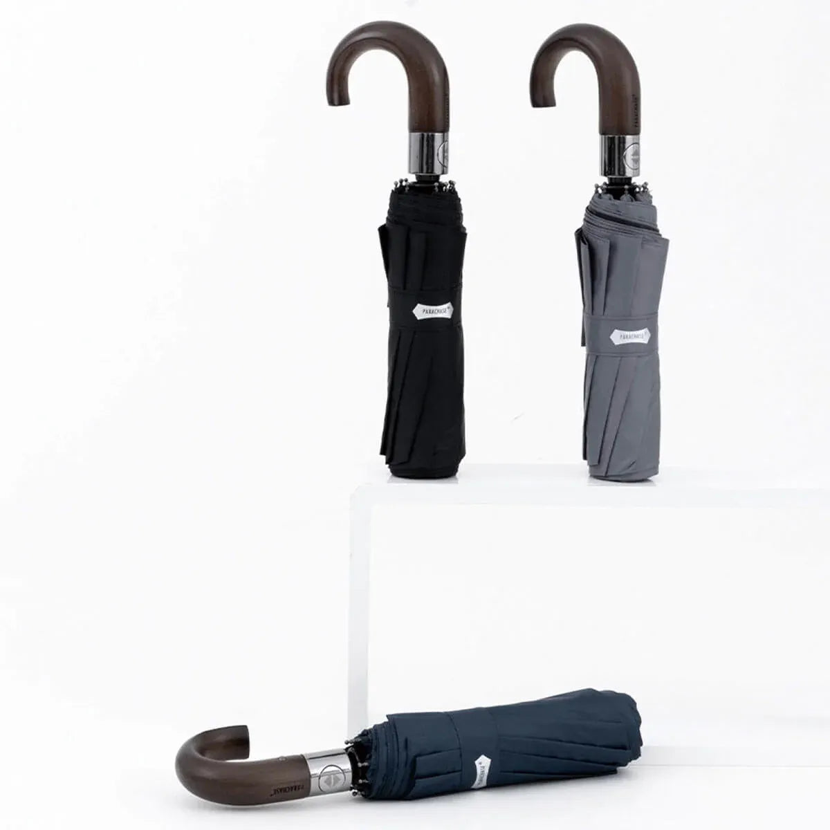 A display of the automatic folding umbrella with wood hook handle in black, grey, and navy colors.