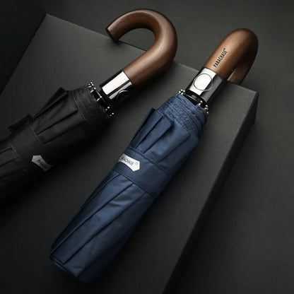Lifestyle shot of the black and navy automatic folding umbrellas with wood handles on a dark surface.