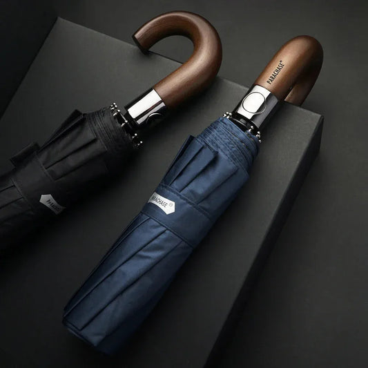 Lifestyle shot of the black and navy automatic folding umbrellas with wood handles on a dark surface.