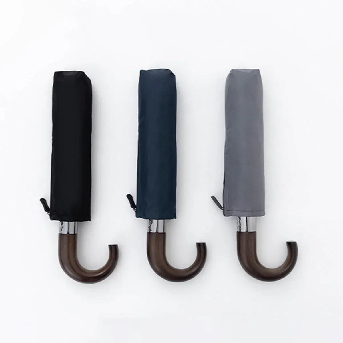 The automatic folding umbrella in black, navy, and grey, shown closed in their carrying sleeves.