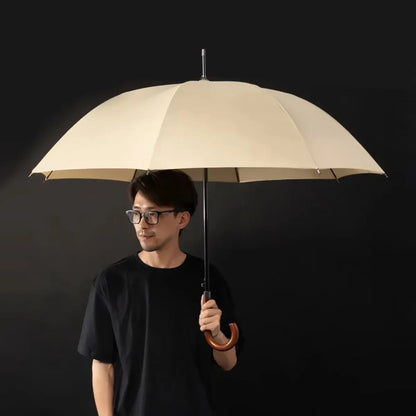A man holding the open beige classic stick umbrella with a wooden crook handle.