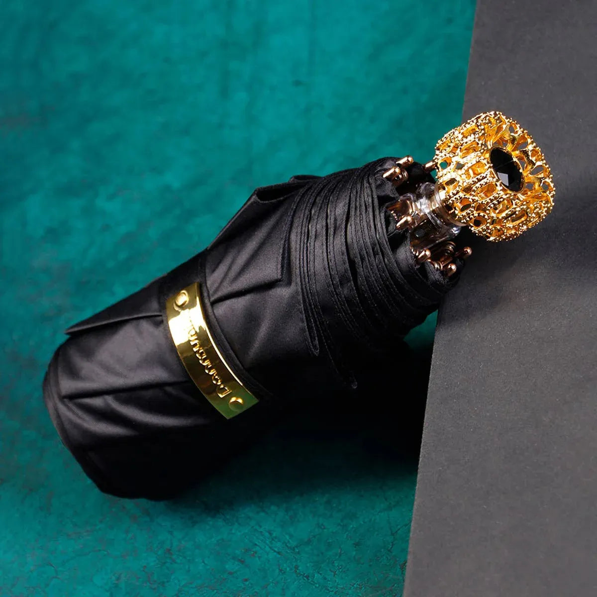 The compact luxury mini umbrella in black, showcasing the ornate golden handle with a black crystal.