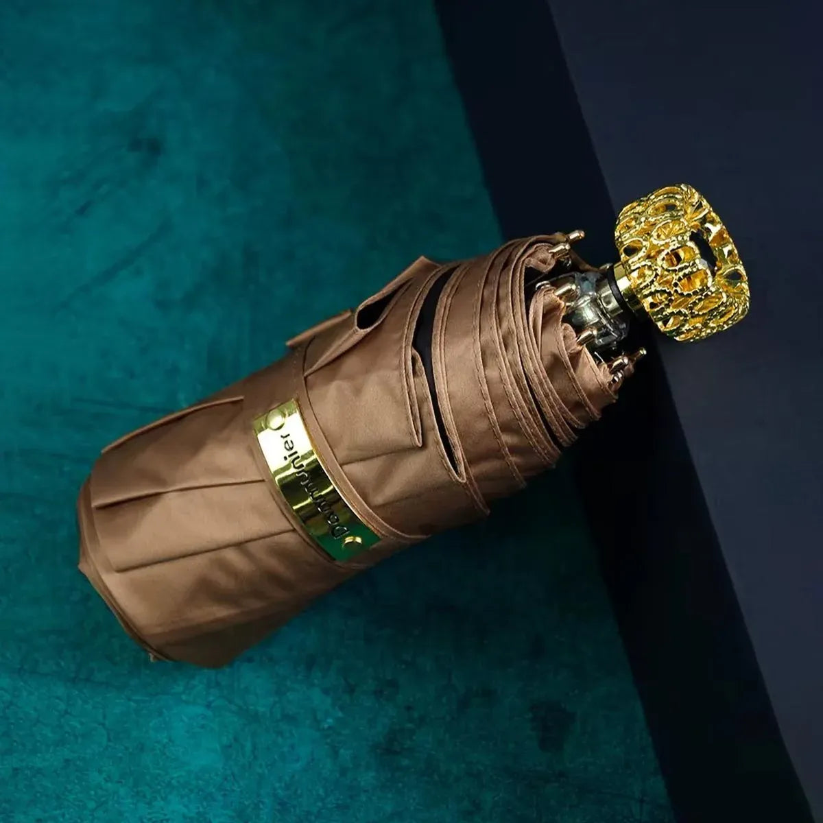 The compact luxury mini umbrella in brown, showcasing the ornate golden handle with a black crystal.