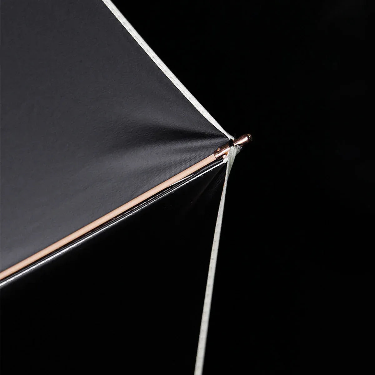 Close-up detail of the canopy tip and golden rib end on the compact luxury umbrella.