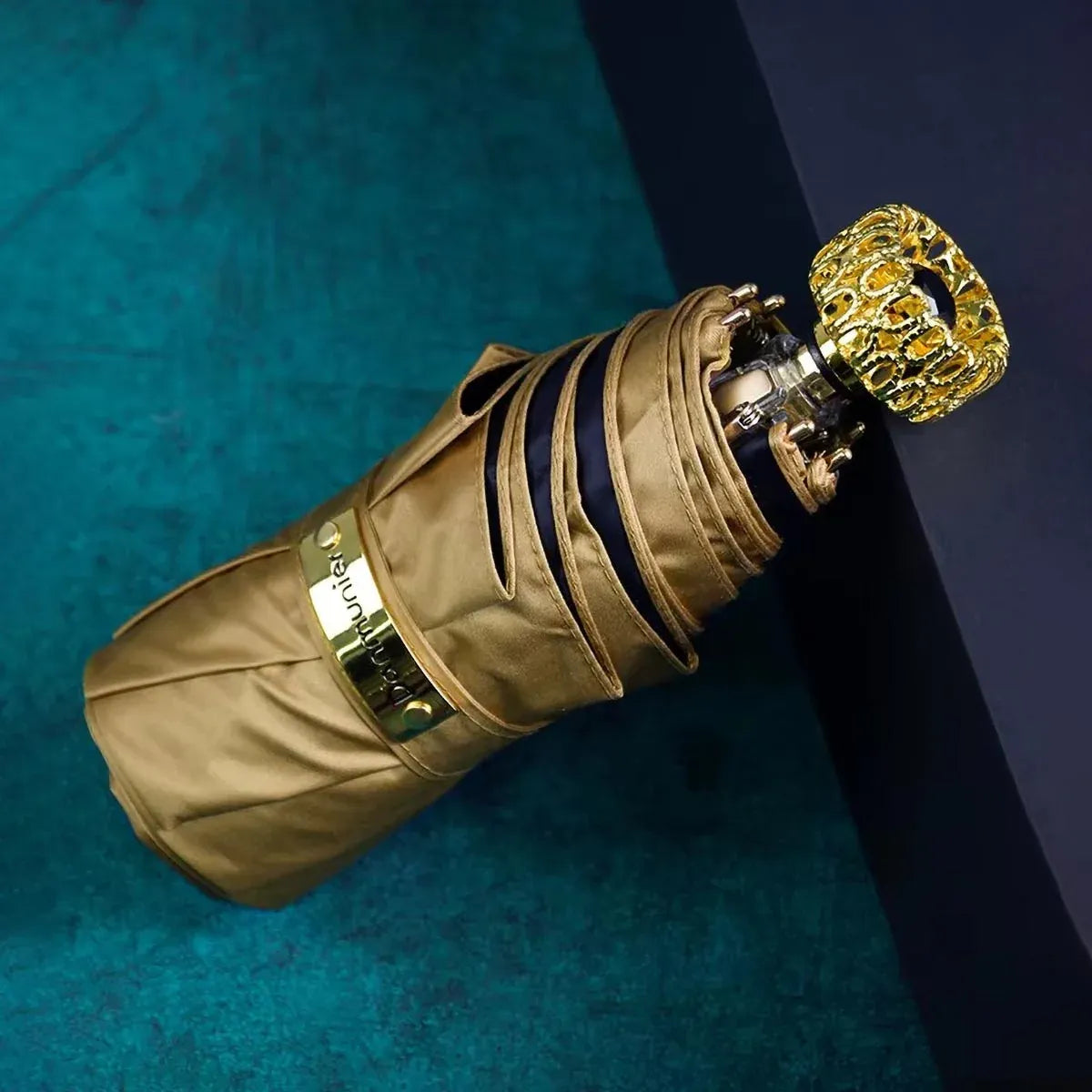 The compact luxury mini umbrella in a gold/khaki color, showcasing the ornate golden handle with a black crystal.