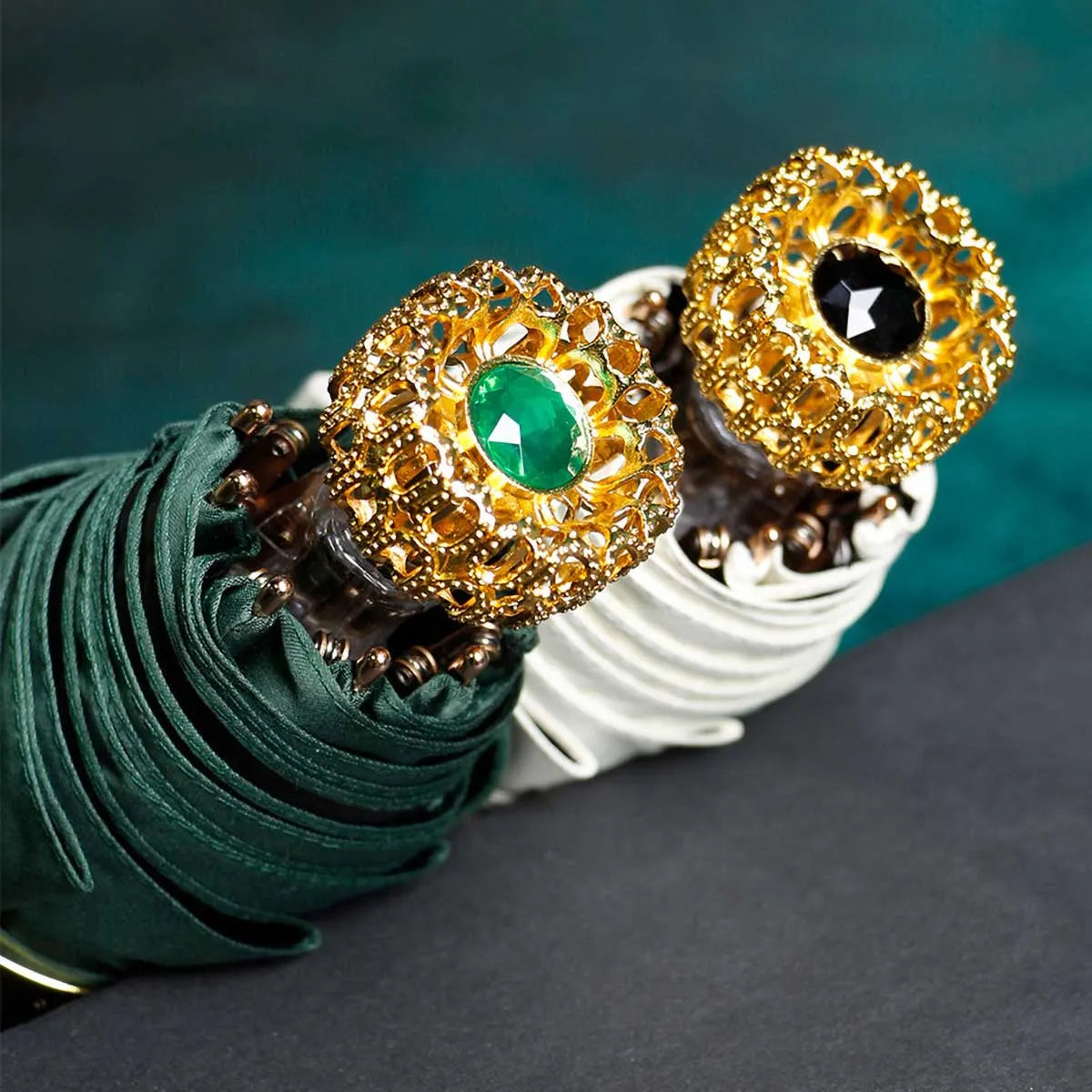 The ornate golden crystal handles of the green and white compact mini umbrellas shown together.