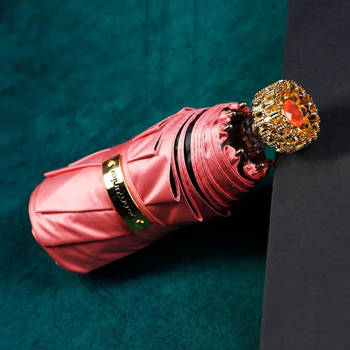 The compact luxury mini umbrella in pink, showcasing the ornate golden handle with a red crystal.