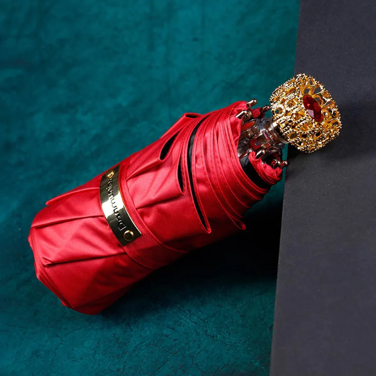 The compact luxury mini umbrella in red, showcasing the ornate golden handle with a red crystal.
