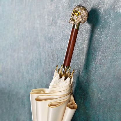 The cream white Diamond Skull stick umbrella leaning against a wall, showcasing the jeweled skull handle.