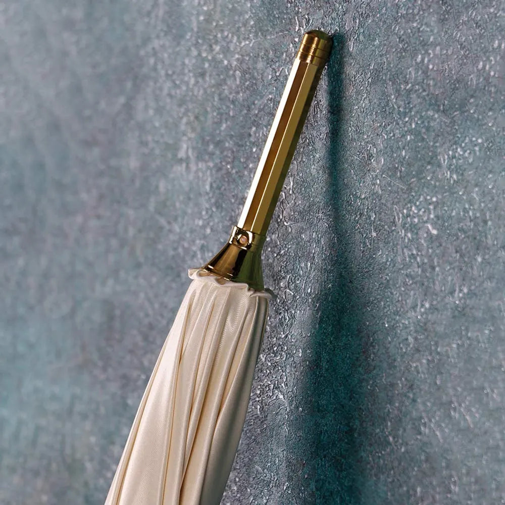 Close-up of the elegant golden metal tip (ferrule) at the bottom end of the closed white umbrella.