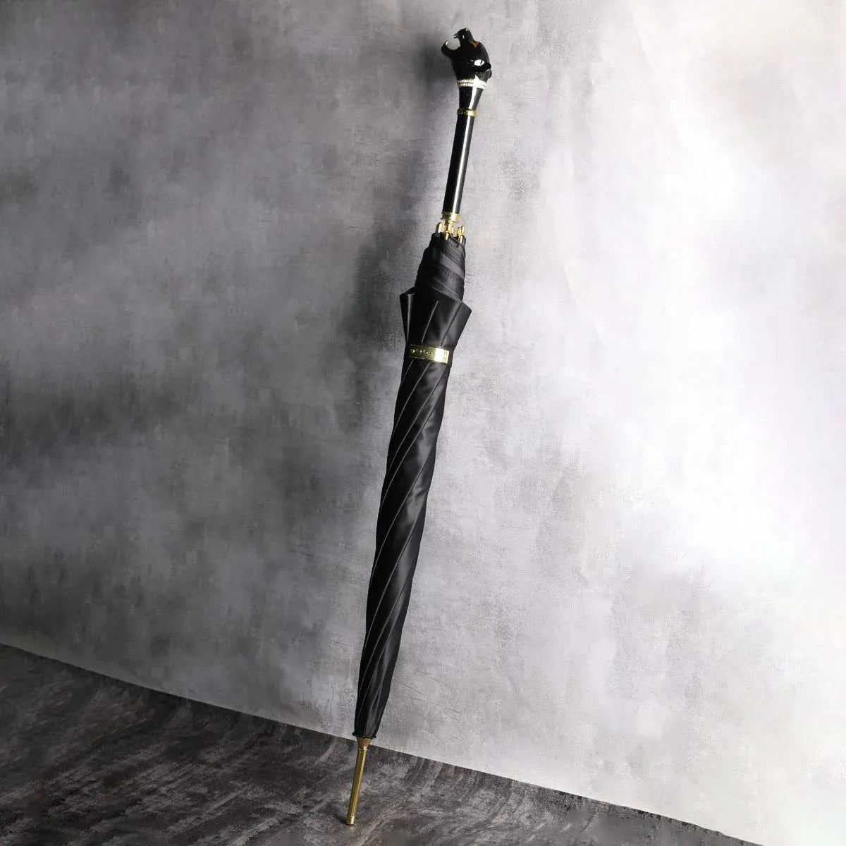 The elegant black stick umbrella with a panther head handle, standing closed against a concrete wall.