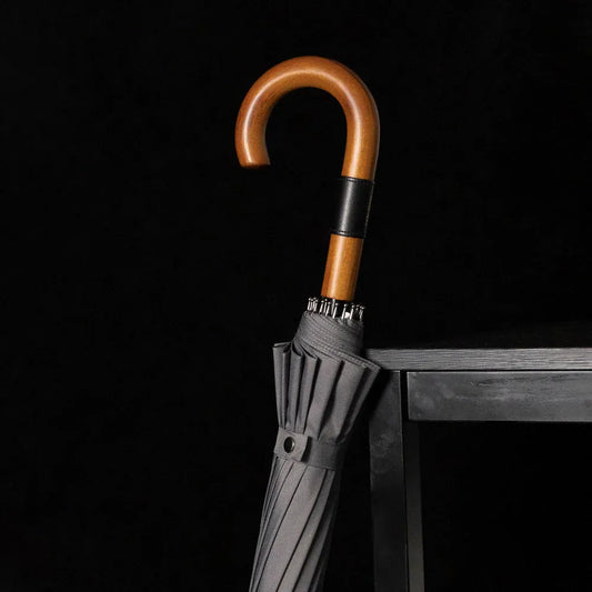 Lifestyle shot of the closed grey 16-rib umbrella with wooden handle resting on a stool.