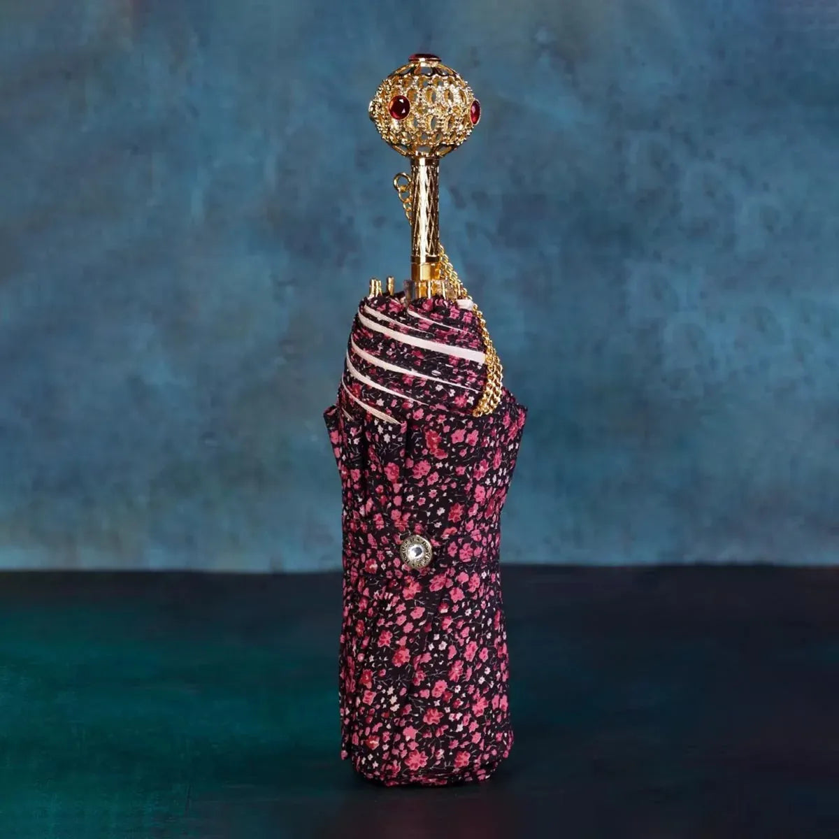 The closed dark floral flower folding umbrella standing upright, showcasing the jeweled handle.