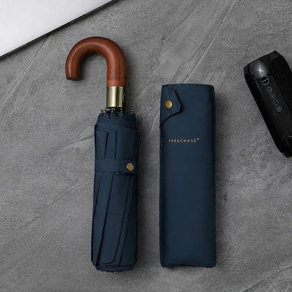 The foldable automatic umbrella with a wooden J-handle in navy blue, shown closed next to its sleeve.