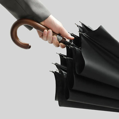 A hand holding the elegant handmade wooden crook handle of the Gentleman's walking umbrella.