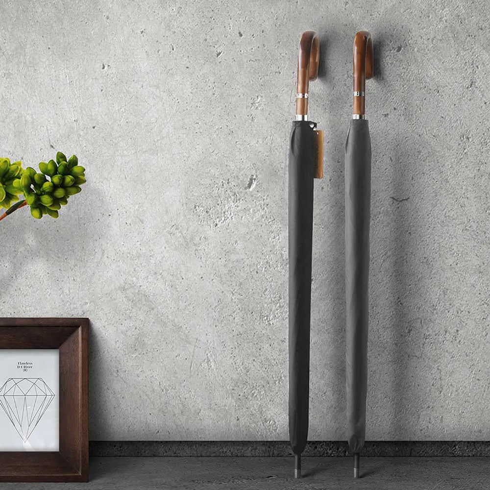 Two closed Gents Black Umbrellas with wooden handles standing against a concrete wall.