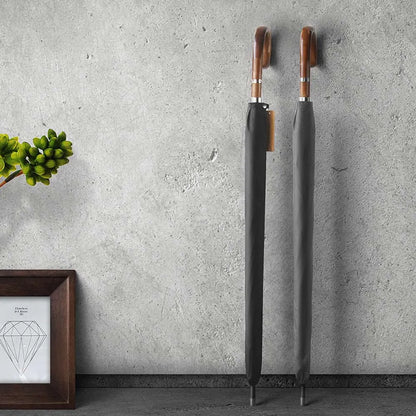 Two closed Gents Black Umbrellas with wooden handles standing against a concrete wall.