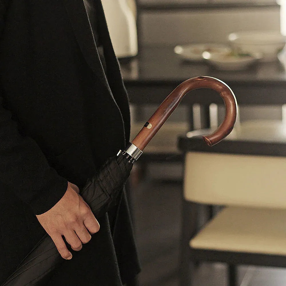 A person holding the closed Gents Black Umbrella by its elegant wooden crook handle.