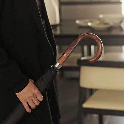 A person holding the closed Gents Black Umbrella by its elegant wooden crook handle.