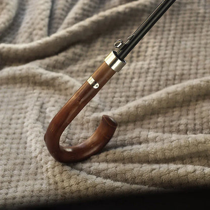 Close-up of the Gents Black Umbrella's wooden crook handle resting on a textured fabric.