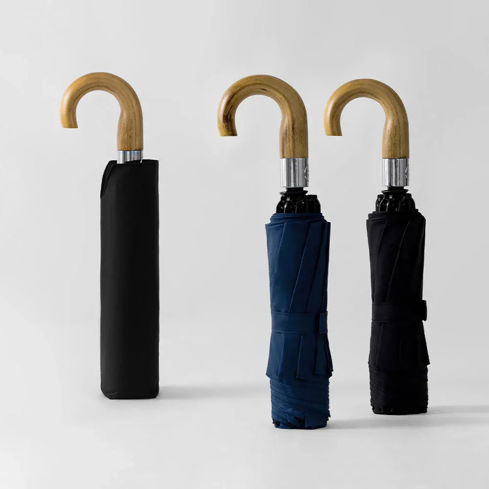 The black, navy, and khaki versions of the inverted umbrella with wooden handles, shown closed.