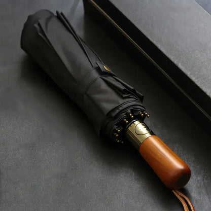 Profile view of the closed black large folding umbrella, highlighting the natural wood handle.