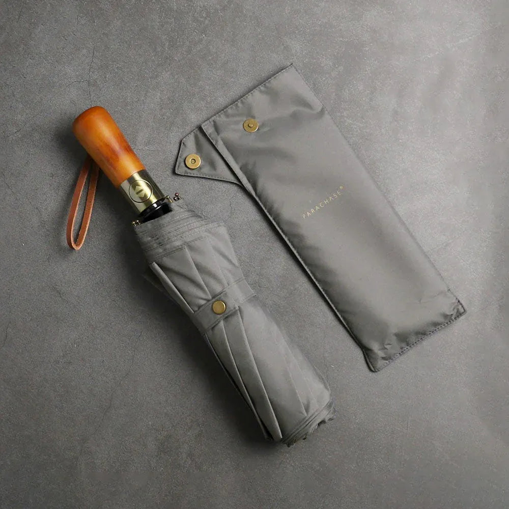 The large automatic folding umbrella with a luxury wood handle in grey, shown closed next to its sleeve.
