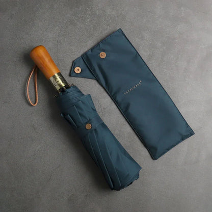 The large automatic folding umbrella with a luxury wood handle in navy blue, shown closed next to its sleeve.
