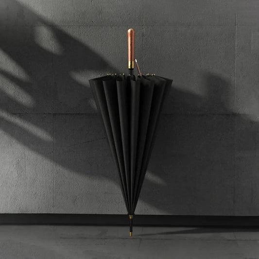 The black 16-rib luxury umbrella standing closed against a dark wall.