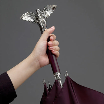 A hand holding the luxurious silver angel handle of the closed burgundy umbrella.