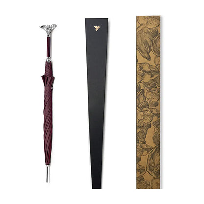 The closed burgundy angel handle umbrella shown alongside its elegant black and patterned packaging.