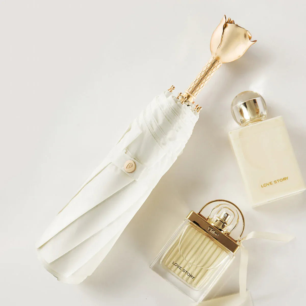 Lifestyle shot of the closed white rose handle umbrella next to perfume bottles.