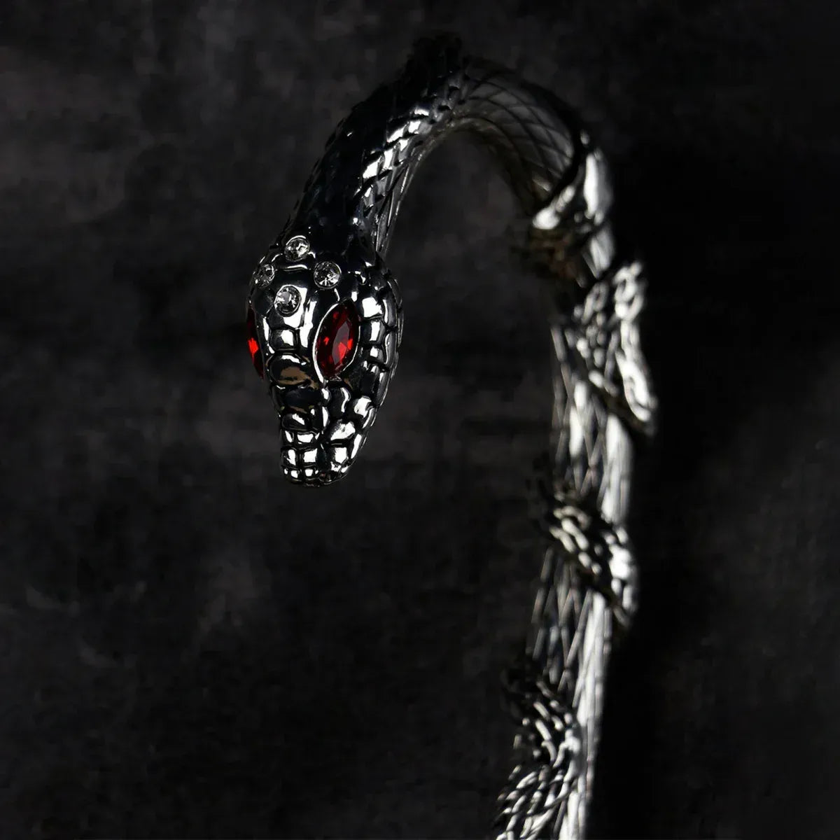 Detailed close-up of the sculpted silver snake handle with red crystal eyes, on the serpent pattern umbrella.