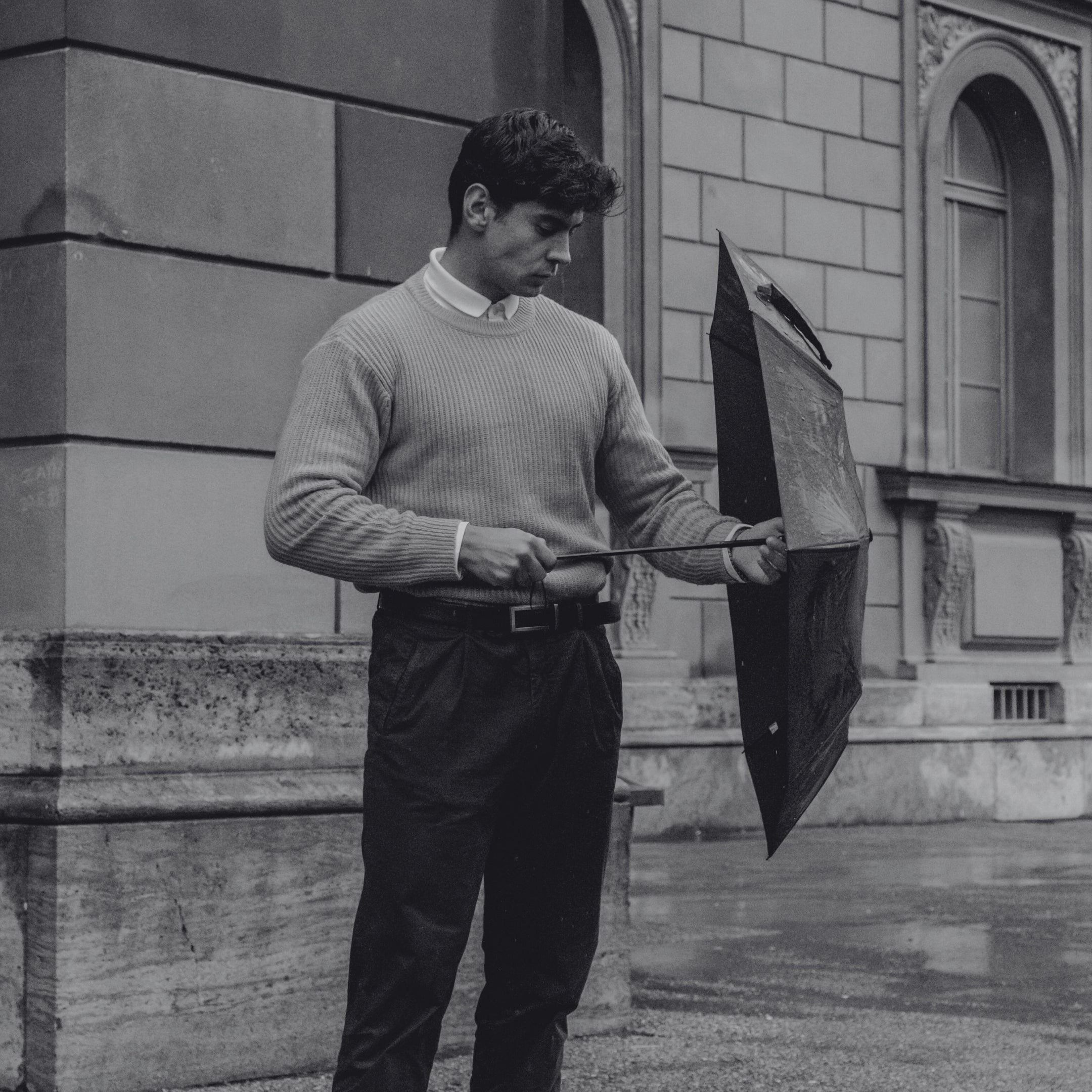 A modern gentleman adjusting his umbrella on a rainy day, representing Exclusaro’s refined and durable luxury umbrellas for men.
