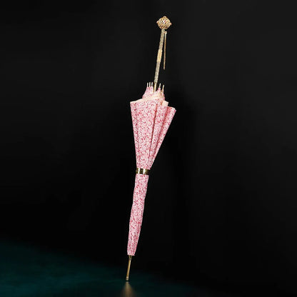 The elegant pink floral stick umbrella standing closed, showcasing its luxury gold handle with chain detail.