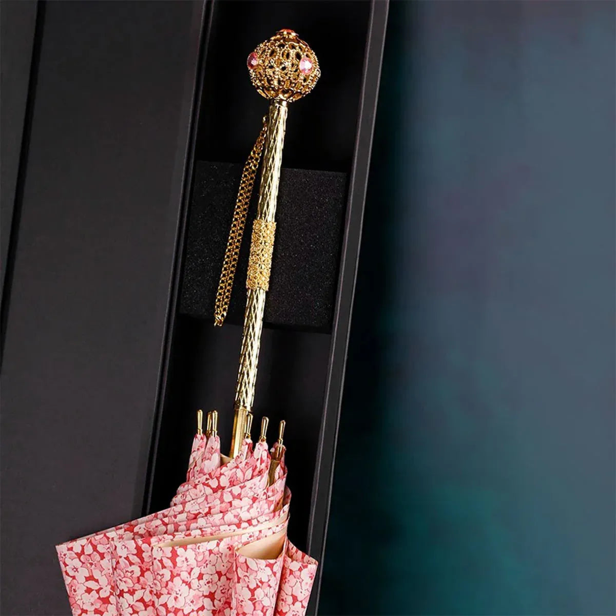 The luxury pink floral umbrella's gold handle shown presented inside elegant packaging.