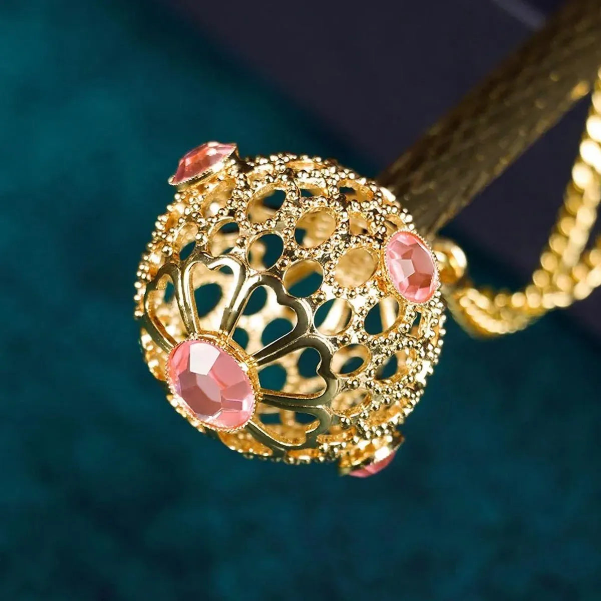 Extreme close-up of the ornate golden handle, showing the intricate filigree metalwork and pink gemstones.