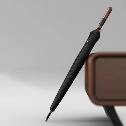 The closed black premium 24-rib windproof umbrella leaning against furniture, showcasing the wood handle.